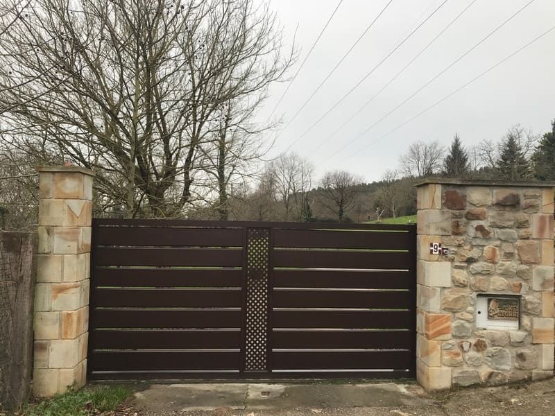 Una puerta marrón está rodeada por un muro de piedra y árboles.