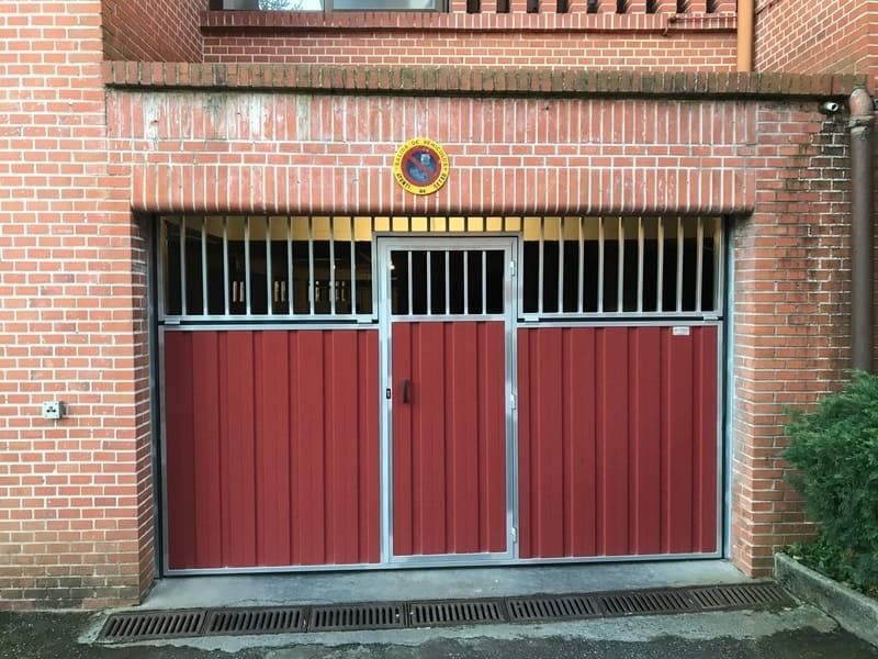 Una puerta de garaje roja está frente a un edificio de ladrillos.