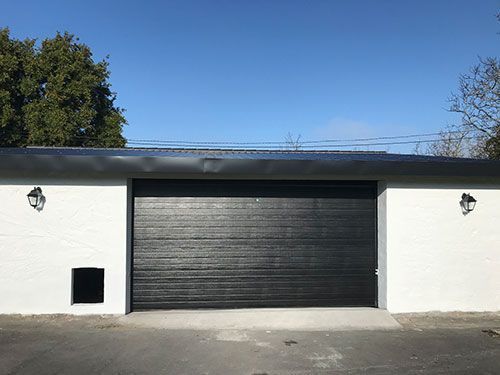 Una puerta de garaje negra está en un edificio blanco.