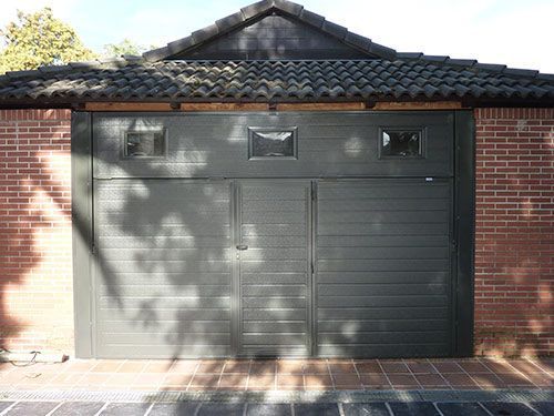 Un garaje de ladrillo con una puerta de garaje negra y un techo de tejas.