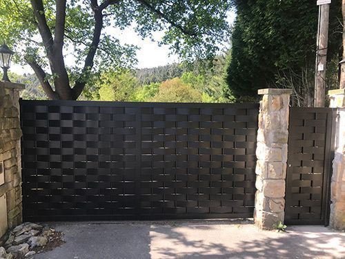 Una puerta negra está rodeada de pilares de piedra y árboles.