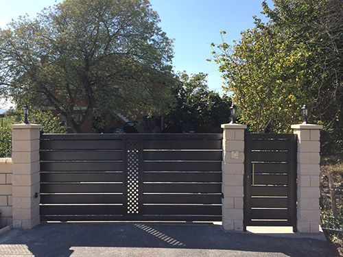 Una puerta negra está rodeada de pilares de ladrillo y árboles.