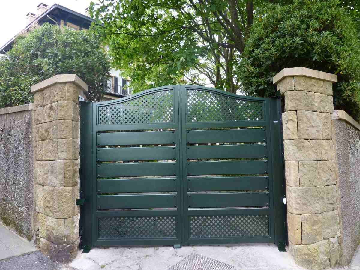Una puerta verde está rodeada de pilares de piedra y árboles.