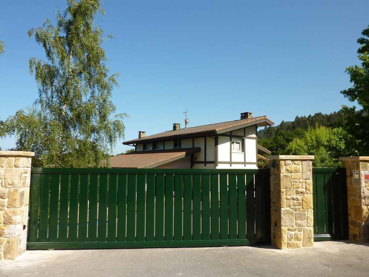 Una casa con una valla verde y un pilar de piedra