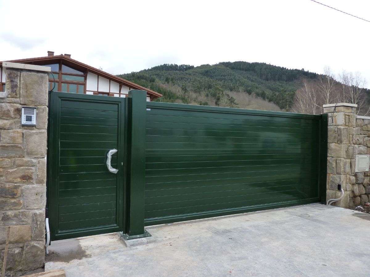 Una puerta verde está frente a una casa con montañas al fondo.