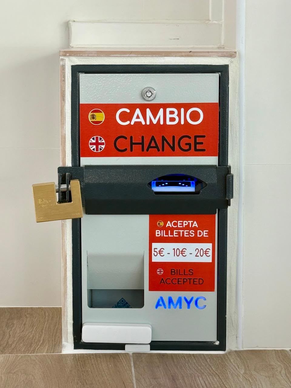 Máquina de cambio de divisas roja y blanca con la etiqueta “CAMBIO/CHANGE” en una pared, con ranuras para monedas y billetes.