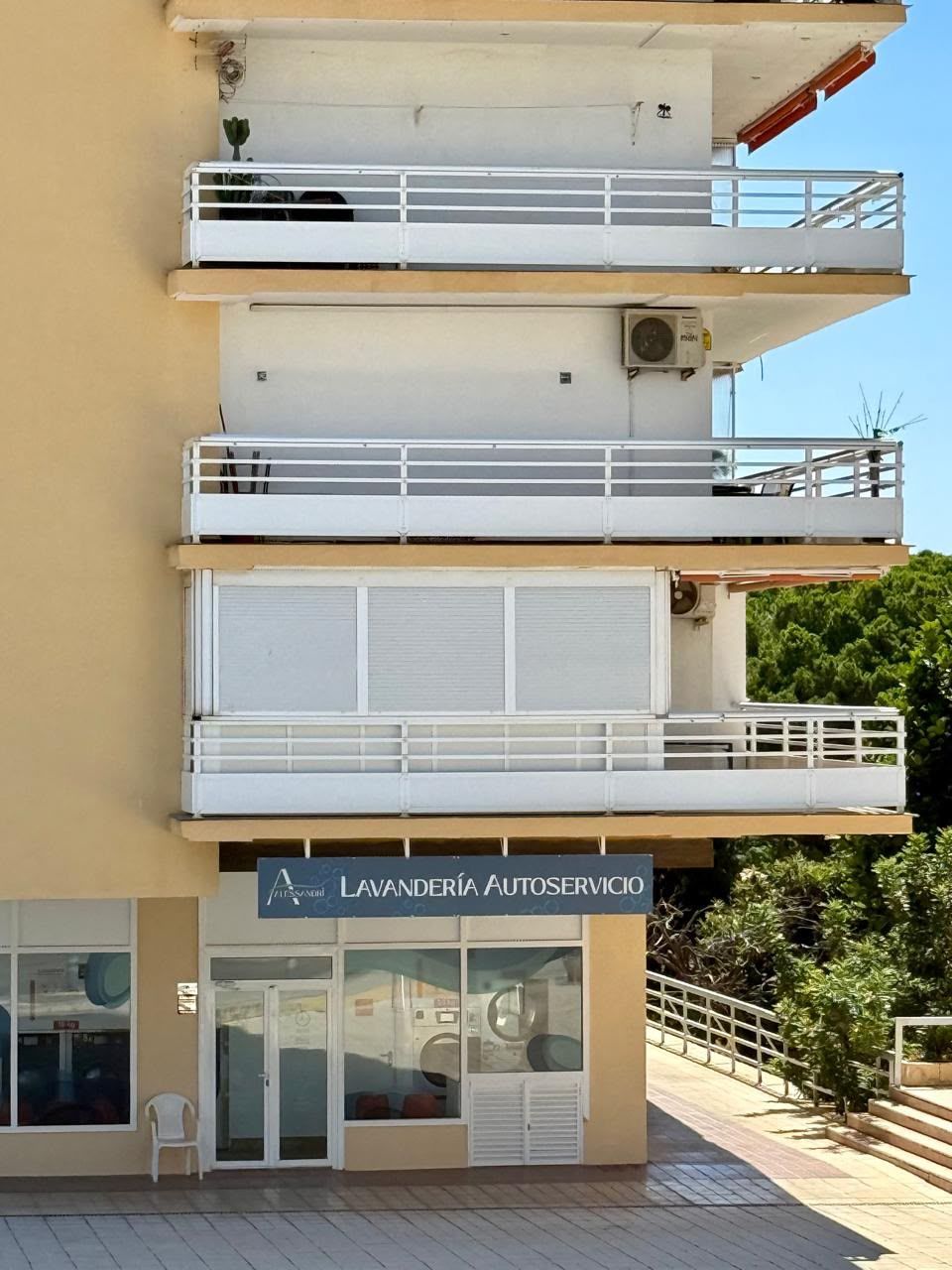 Edificio de apartamentos con balcones sobre un local comercial, fachada beige y barandillas blancas.
