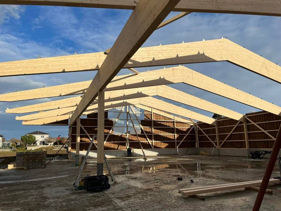 Construction de la charpente en bois d'un toit, avec ses multiples poutres inclinées, sous un ciel nuageux.