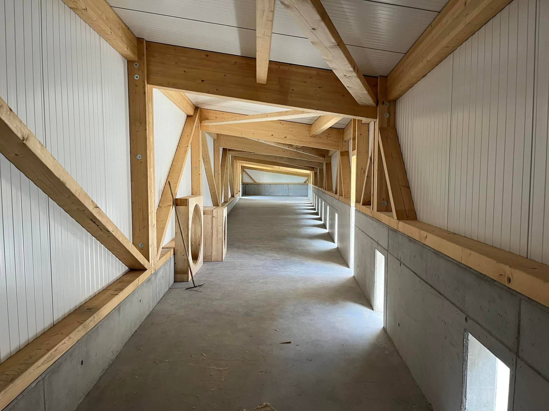 Intérieur d'un bâtiment en construction, montrant les poutres en bois, le sol et les murs en béton, et l'isolation.