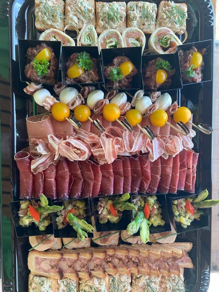 Disposition d'amuse-gueules : viandes, brochettes et diverses petites bouchées sur un plateau noir.