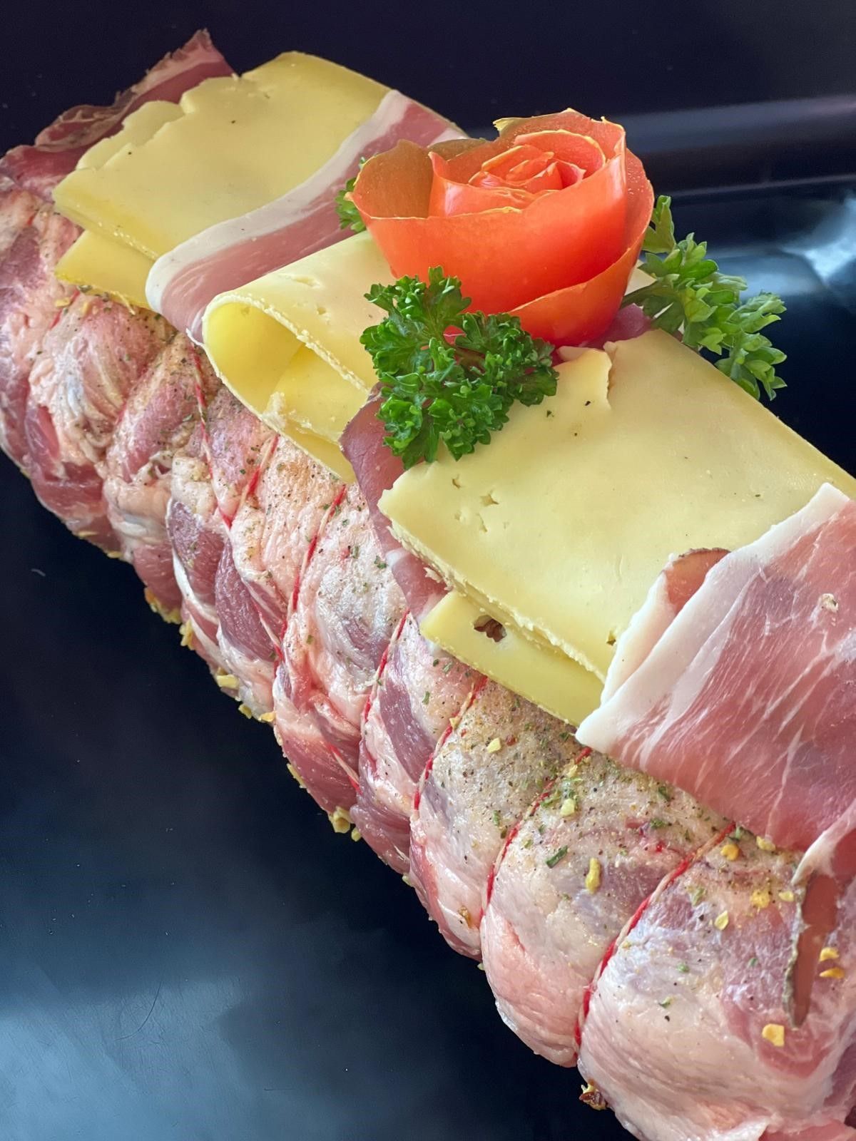 Pain de viande enveloppé de bacon, garni de fromage, de tranches de bacon, de rose de tomate et de persil.