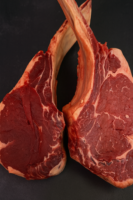 Deux steaks de tomahawk crus avec os sur une surface sombre.