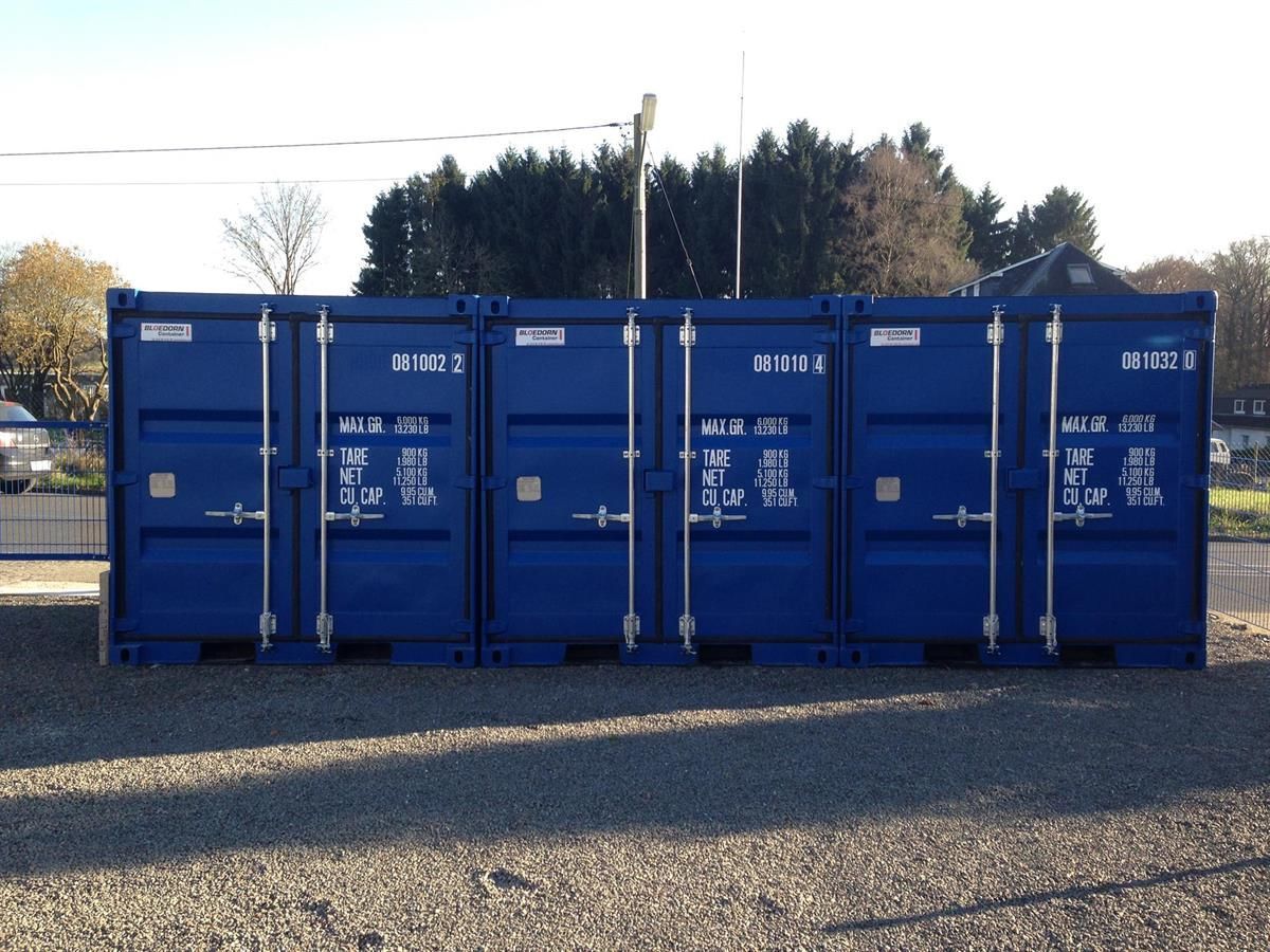 Eine Reihe von blauen Schiffscontainern stehen auf einem Kiesplatz