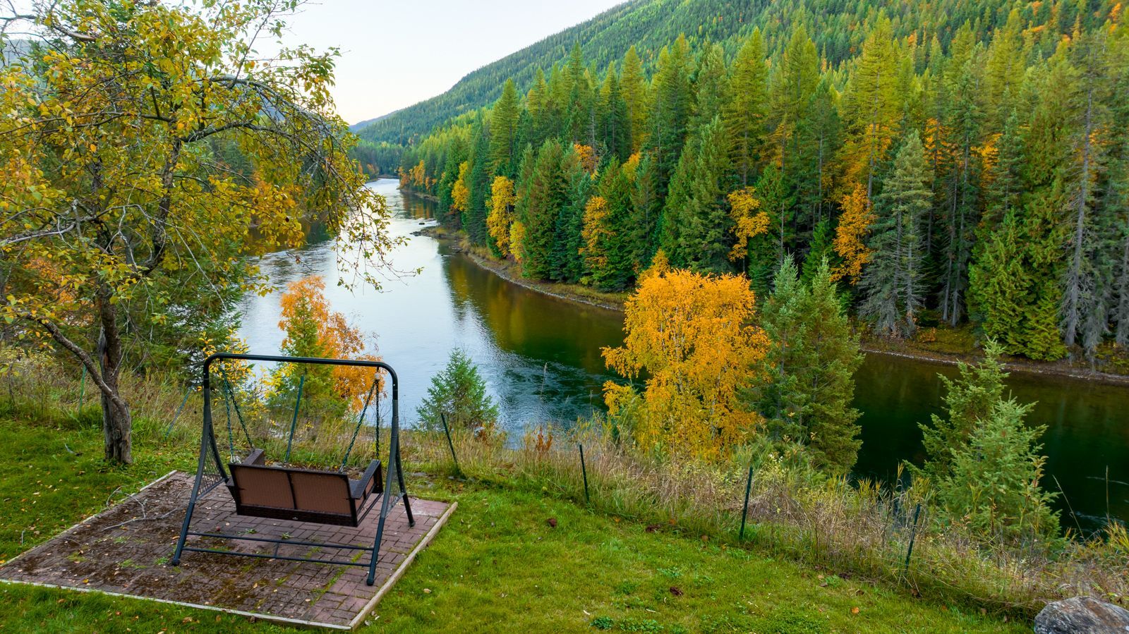 A rustic interior featuring a wooden ceiling, a large wall clock above a dark wood console table, and a staircase.