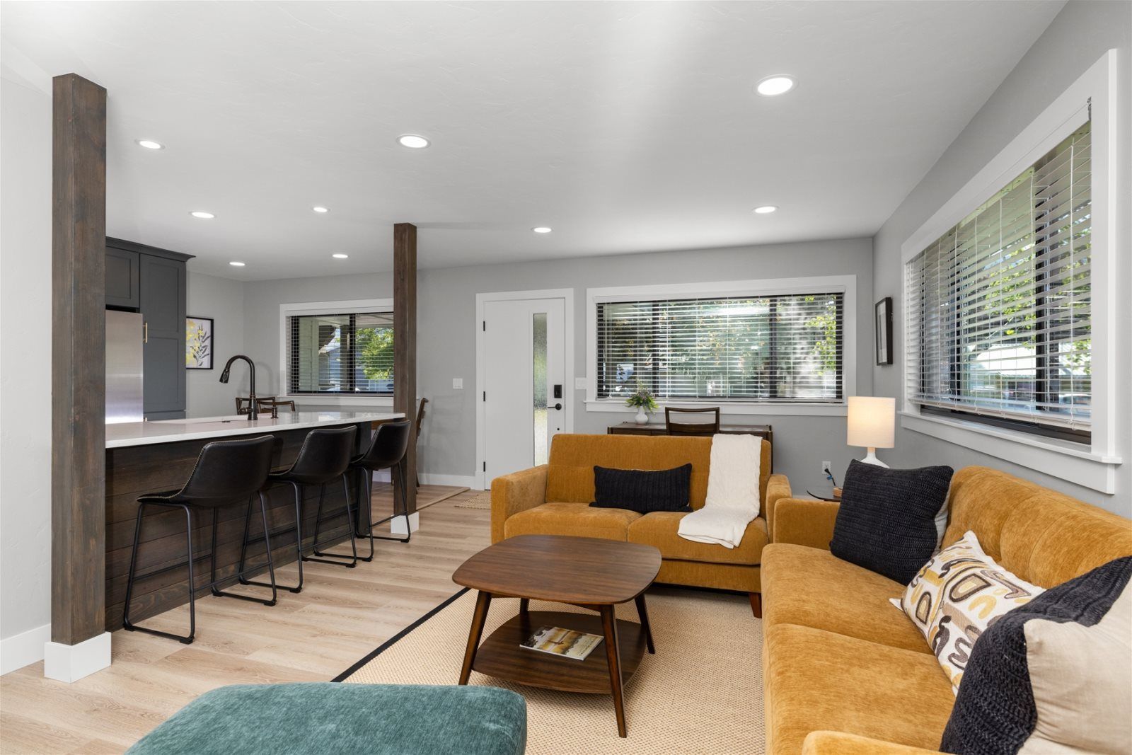 Open-concept living room and kitchen featuring yellow couches, a wooden coffee table, and a kitchen island with bar stools.