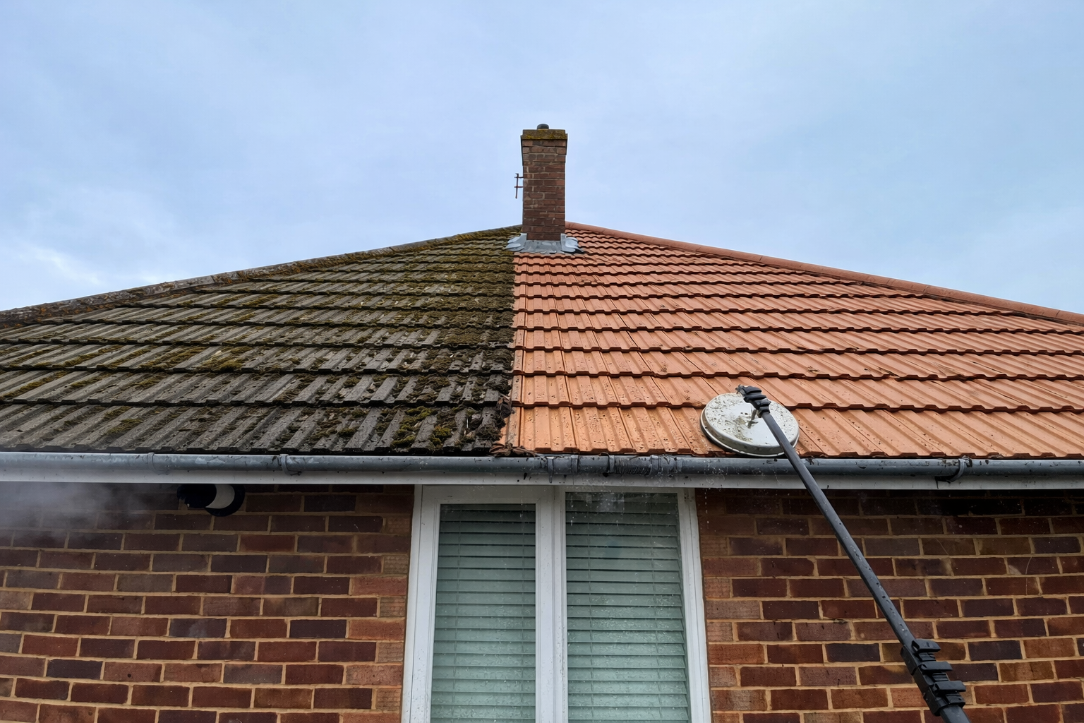 House roof with half dark mossy tiles and half red tiles, with a satellite dish and chimney.