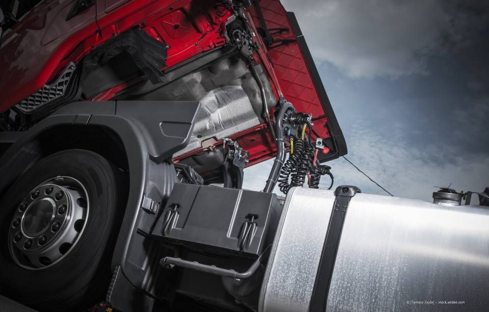 Sattelschlepper mit offener Motorhaube. Rotes Fahrerhaus mit einem Mechaniker, der am Motor arbeitet. Bewölkter Himmel.