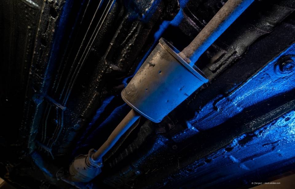 Unterseite eines Autos mit schwarz lackierter Auspuffanlage und Boden. Blaues Licht hebt die Teile hervor.