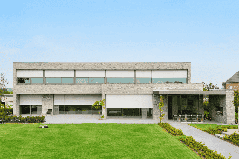 Moderna casa de ladrillo con grandes ventanales, persianas automáticas y césped verde.