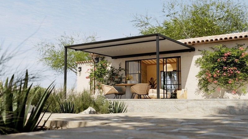 Un patio con toldo retráctil, con asientos al aire libre frente a un edificio con puertas de vidrio, rodeado de plantas.