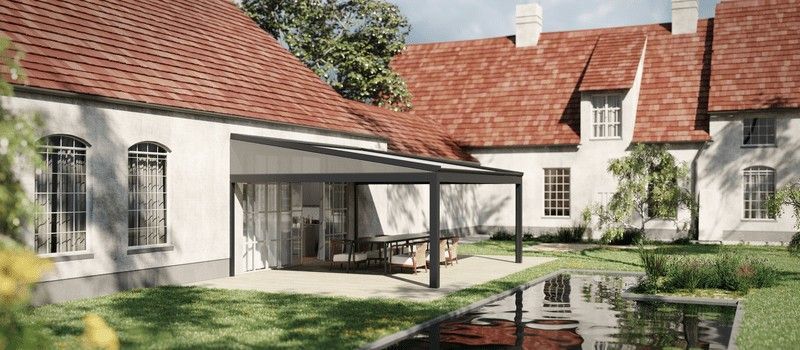 Vista exterior de una casa blanca con techo de tejas rojas, con un patio cubierto sobre un patio de piedra