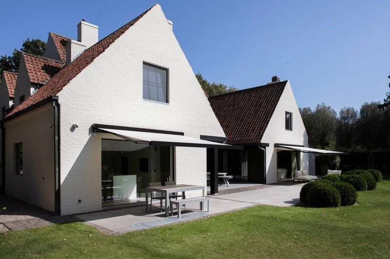 Casa de ladrillo blanco con techo de tejas rojas, puertas de vidrio, patio, toldo y césped.