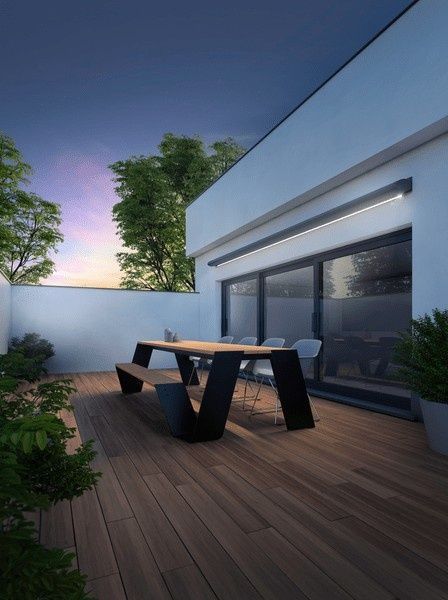 Patio al aire libre con terraza de madera, mesa moderna de madera y negra y exuberante vegetación al anochecer.