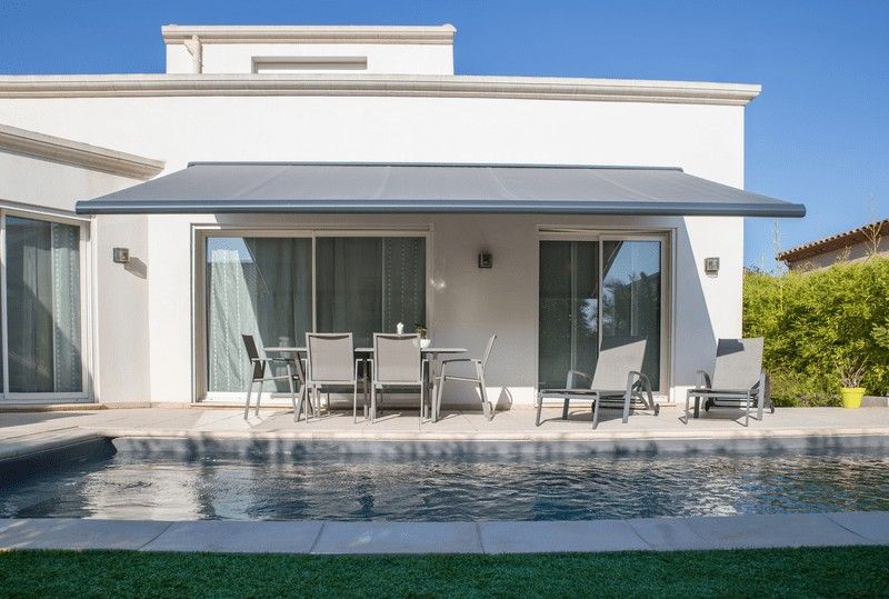 Una casa moderna con piscina y muebles de patio a la sombra de un toldo retráctil.