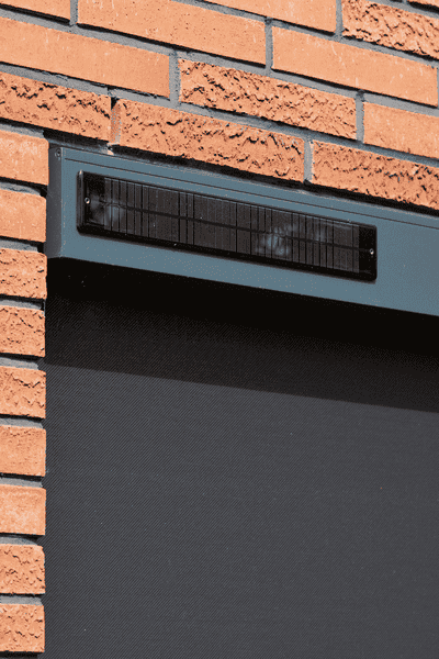 Respiradero oscuro situado en un panel horizontal azul, sobre una pared de ladrillos.