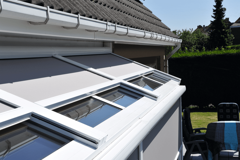 Techo blanco de solárium con persiana retráctil y ventanas de cristal. Molduras blancas y techo gris oscuro.