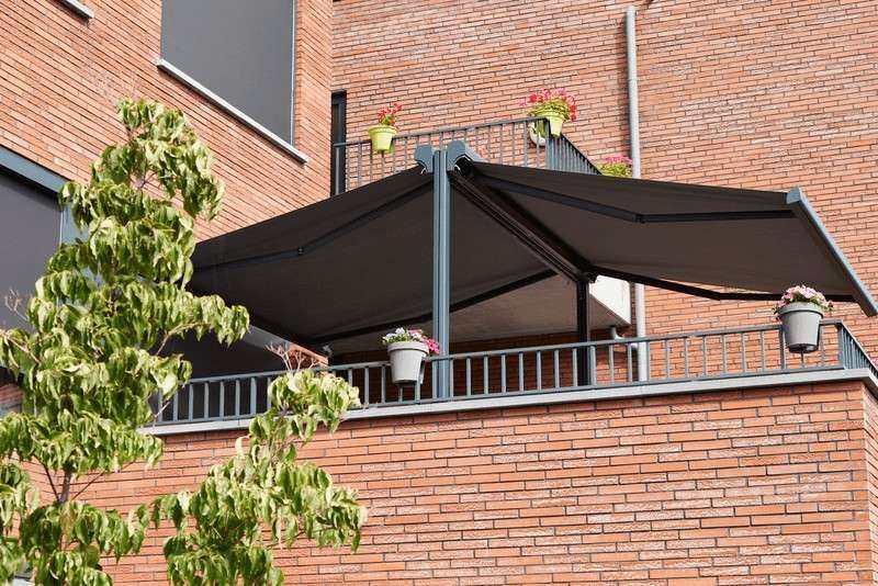 Balcón con toldo gris oscuro, edificio de ladrillo y plantas en macetas.