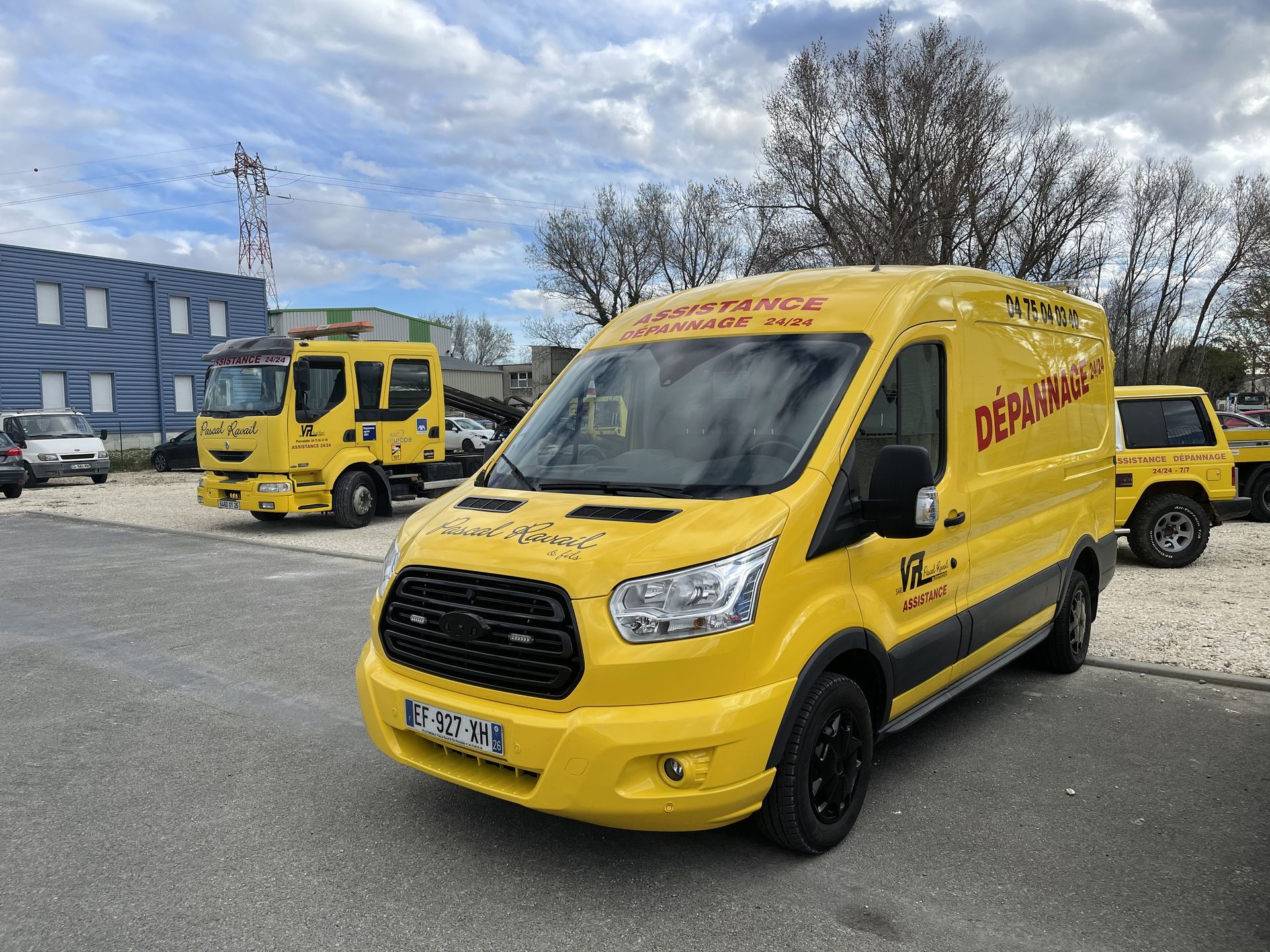 Une camionnette jaune et des dépanneuses sont stationnées devant un bâtiment. L'inscription « DÉPANNAGE » figure sur le côté de la camionnette.