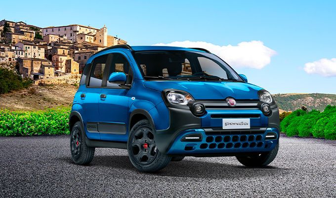 Un SUV Fiat Panda Cross bleu sur une route, avec une ville et de la verdure en arrière-plan.