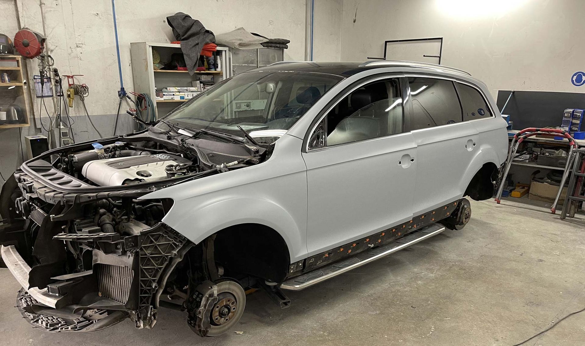 SUV dans un atelier de carrosserie, partiellement démonté, apprêté en gris, avec toit et marchepieds latéraux noirs.