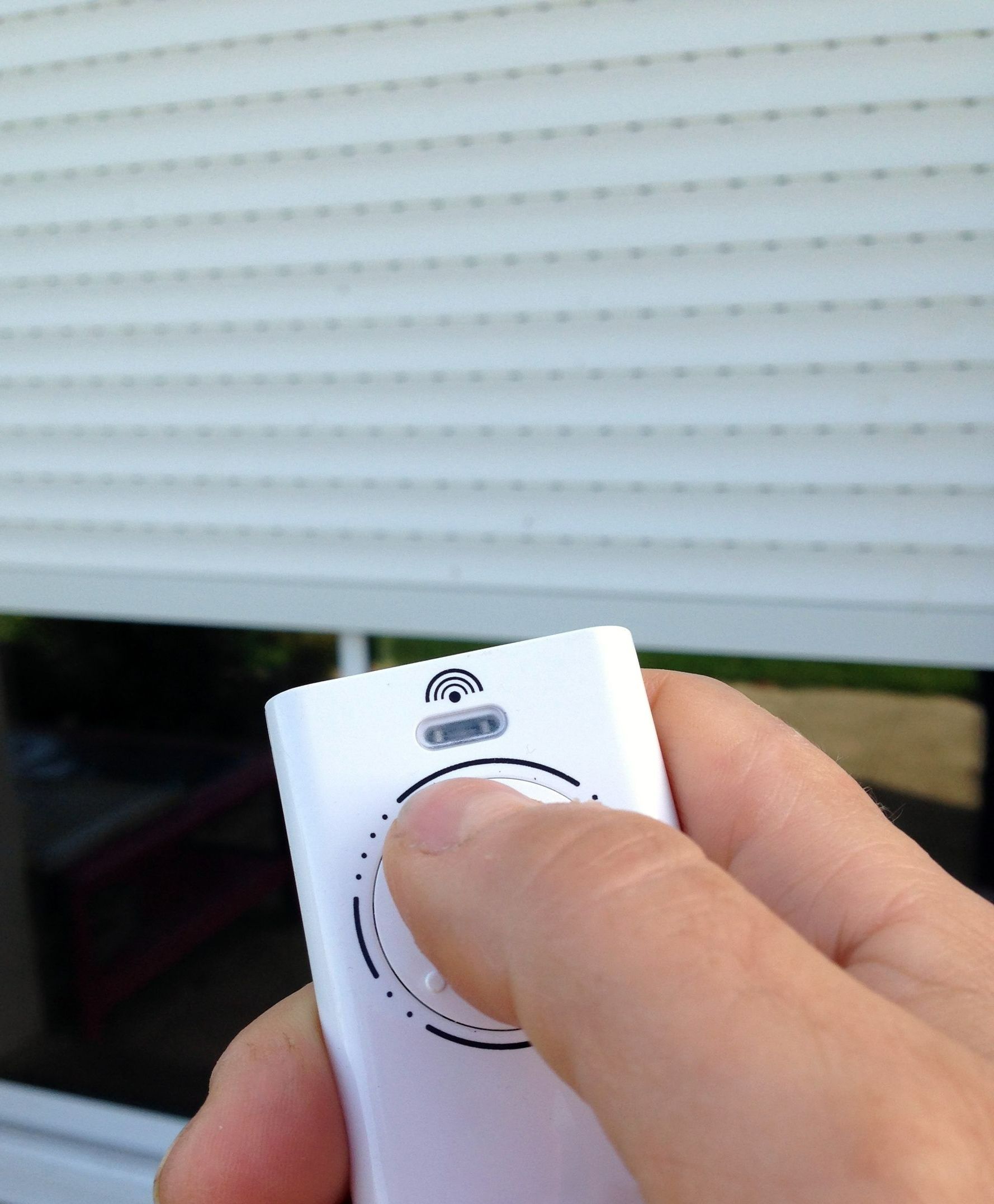 Une main pointe une télécommande face à un volet roulant électrique