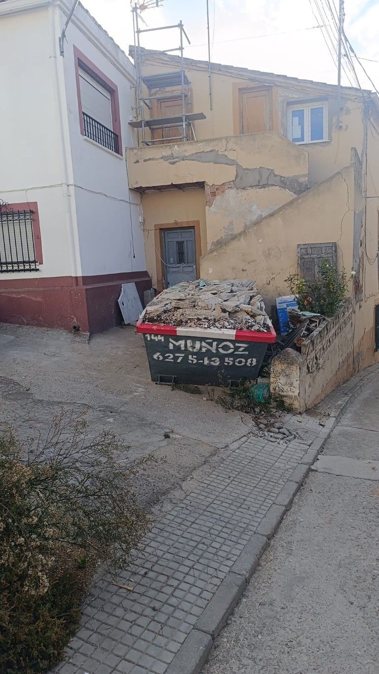 Un contenedor de basura desbordado se encuentra en un callejón estrecho junto a edificios desgastados