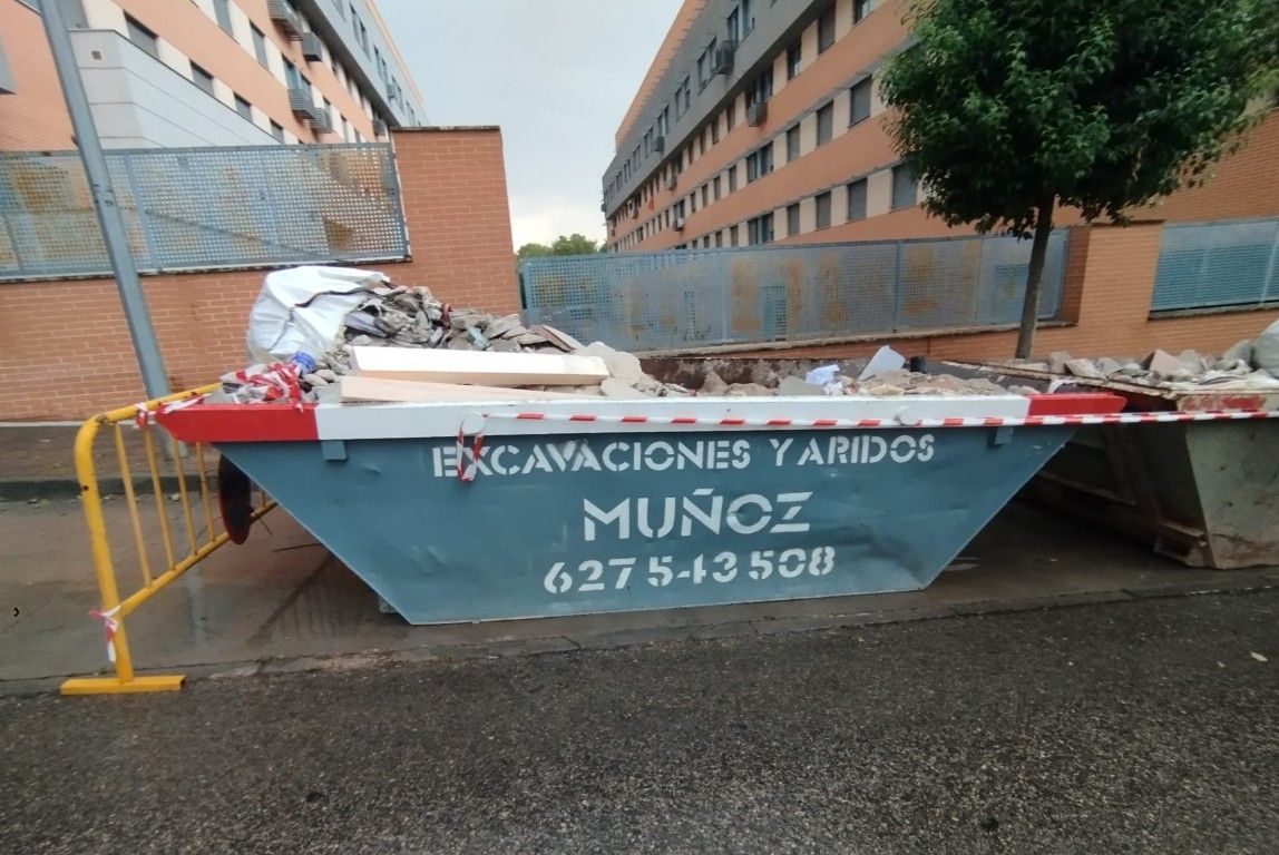 Contenedor azul para escombros de demolición en una calle entre edificios de apartamentos.