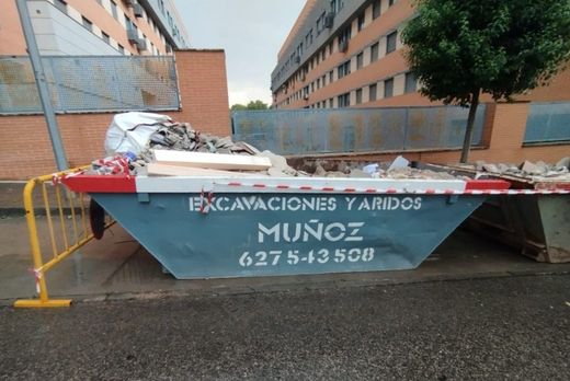 La pala de una excavadora está removiendo tierra marrón en una obra de construcción, con montones de tierra en primer plano.