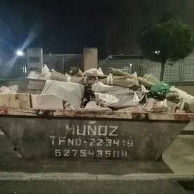 Un contenedor de basura desbordado de escombros y desperdicios por la noche, con la etiqueta 
