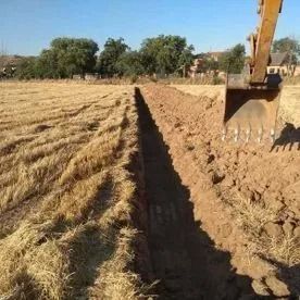 Una excavadora cava una zanja junto a un campo cosechado bajo un cielo despejado.