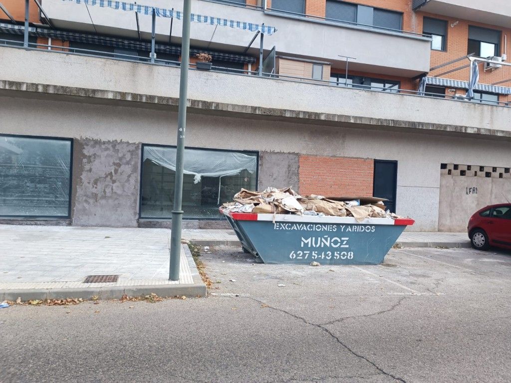 Contenedor de basura en la calle, frente a un edificio, con la etiqueta 
