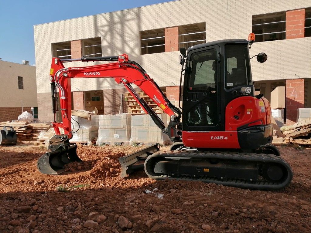 Excavadora naranja cavando en una zanja fangosa, vista desde atrás en una pendiente de tierra pronunciada.