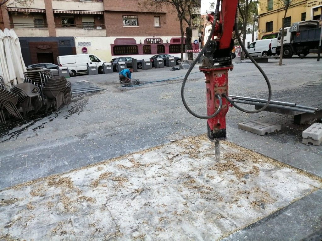 Un equipo de construcción perfora hormigón en una calle de la ciudad, con un martillo neumático rojo y escombros esparcidos.
