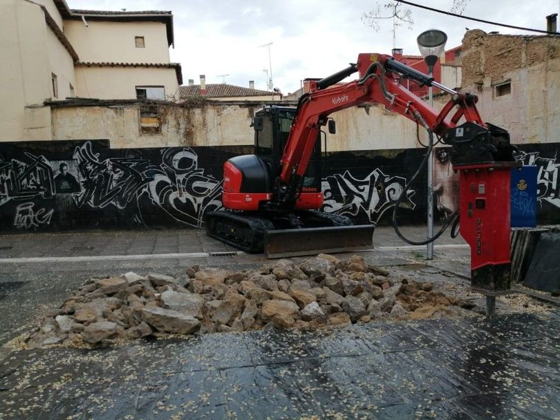 Contenedores de obra verdes en una calle con un camión amarillo y edificios de apartamentos al fondo.