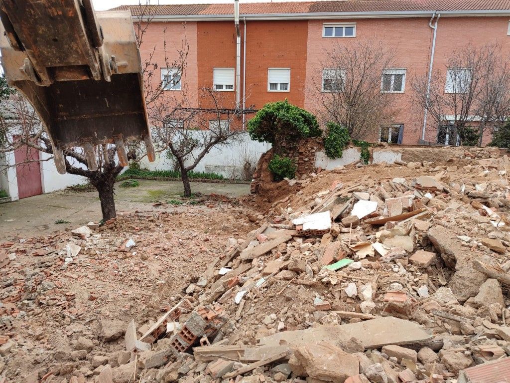 Escombros y restos derrumbados en un patio junto a un edificio de ladrillo y una estructura metálica.
