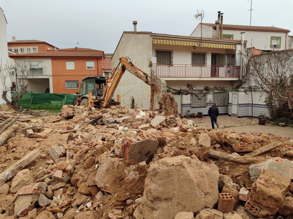 Una excavadora retira los escombros junto a las casas dañadas tras el derrumbe de un edificio, con una persona de pie cerca.