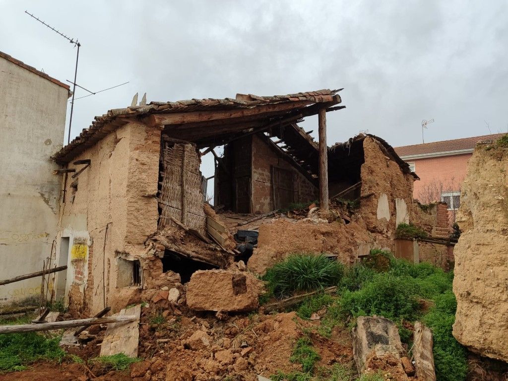 Ruinas de casas de adobe derrumbadas junto a otros edificios bajo un cielo gris.