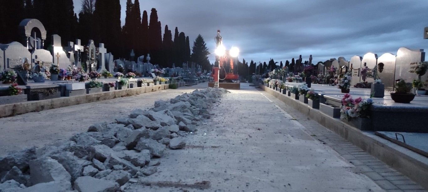 Sendero nevado en un cementerio al anochecer, con hileras de tumbas y faroles a ambos lados.