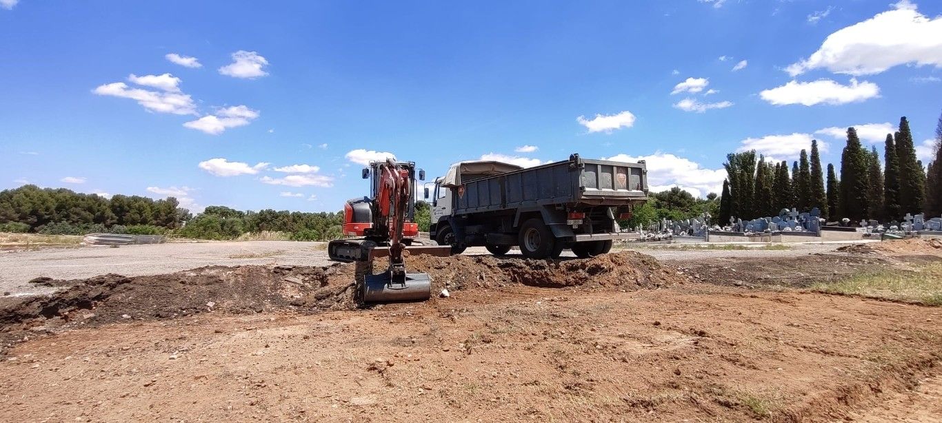 Excavadora y camión volquete en una obra de construcción de tierra bajo un cielo azul.