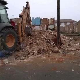 Retroexcavadora retirando escombros de un edificio demolido junto a una carretera.